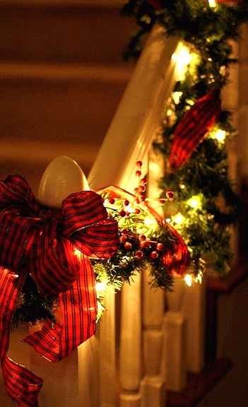 an evergreen and light garland with red berries and a red plaid bow is a cool way to style railing, a mantel or window