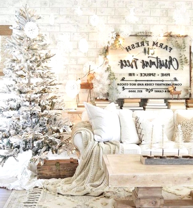 a winter wonderland Christmas living room with a flocked Christmas tree with lights, neutral furniture and linens, a Christmas sign with trees and lights