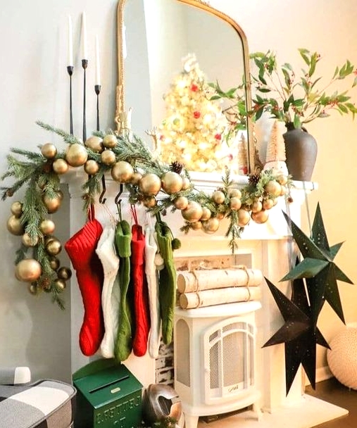 a pretty Christmas mantel in traditional colors, with an evergreen and gold ornament garland, red, green and white stockings