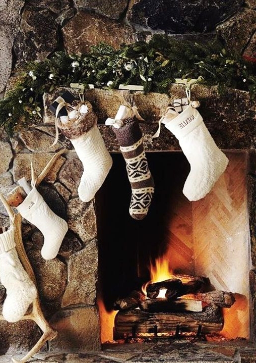 a woodland hearth with white and brown knit stockings, antlers, pinecones, evergreens and ornaments is a very cozy nook