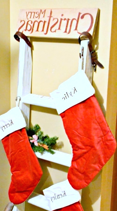 a ladder with classic red and white stockings and a sign on top is a simple and pretty rustic decoration for Christmas