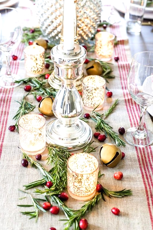 a beautiful Christmas centerpiece with greenery, berries, mercury glass candleholders, large bells and a striped runner