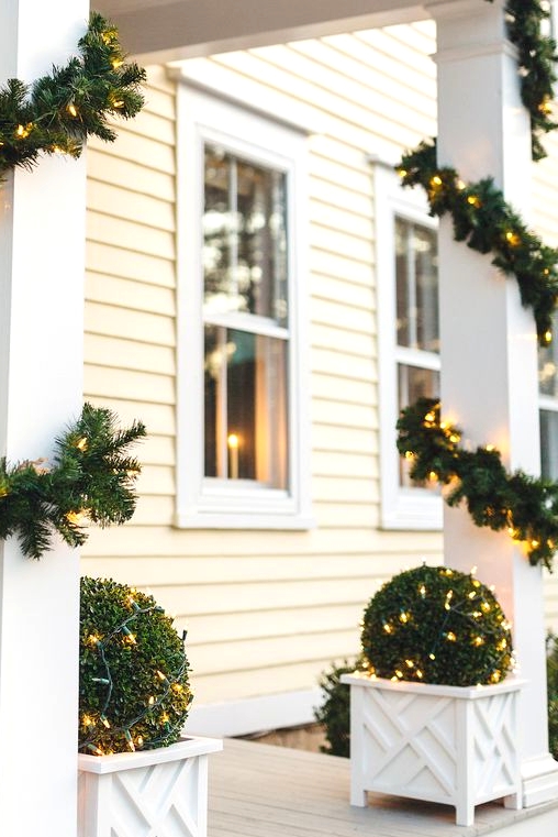 evergreen and light garlands covering the pillars and matching lit up topiaries in white planters make the space awesome