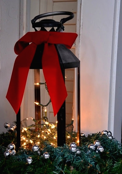 a basket with evergreens, ornaments, a lantern with lights and a red bow on top compose great decor for Christmas