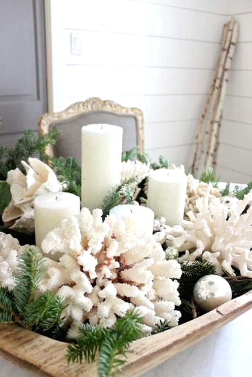 a beach Christmas centerpiece of a wooden bowl, with evergreens, corals, pillar candles, silver and pearl-colored ornaments is amazing