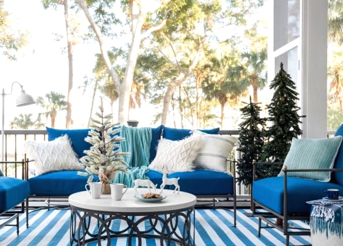 a blue and white coastal Christmas terrace with blue furniture, neutral pillows, Christmas trees, deer and a striped rug