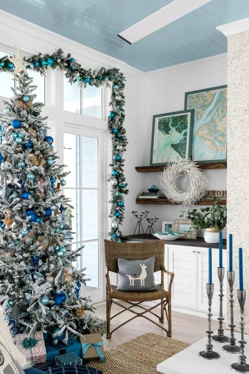 a gorgeous coastal Christmas space with an evergreen and turquoise ornament garland, a flocked Christmas tree with light blue and electric blue ornaments