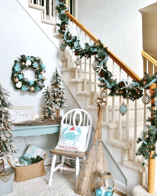 a fantastic beach Christmas nook with an evergreen wreath with ribbons and metallic ornaments and a matching garland on the railing, flocked Christmas trees and a candle lantern with ornaments