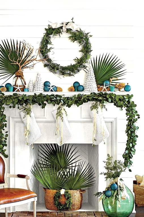 beach Christmas space with a greenery garland and a wreath, tropical leaves, teal Christmas ornaments and mini trees