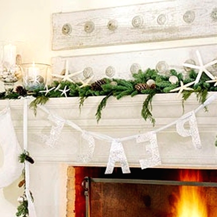 a beach Christmas mantel with evergreens, pinecones, starfish, glasses with seashells and pillar candles, a letter bunting, stockings