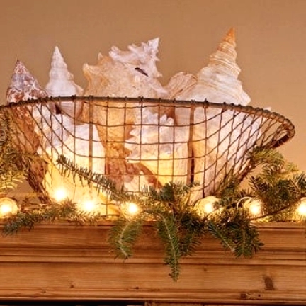 a wire basket with oversized seashells, lights and evergreens around is a gorgeous beach Christmas decoration or centerpiece