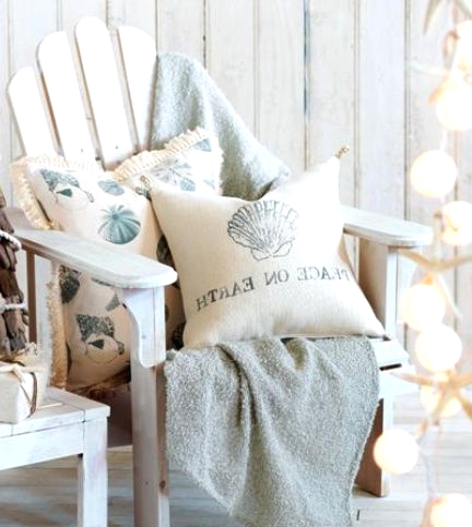 a neutral and pastel beach Christmas nook with a white planked chair, a light blue blanket, printed pillows and a garland