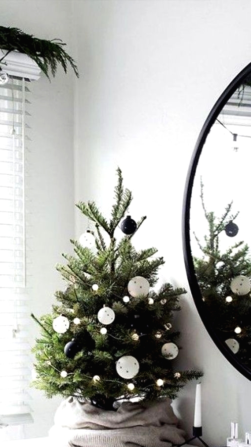a modern Christmas tree decorated with blak and white ornaments and pompom lights plus an old sweater as a tree skirt