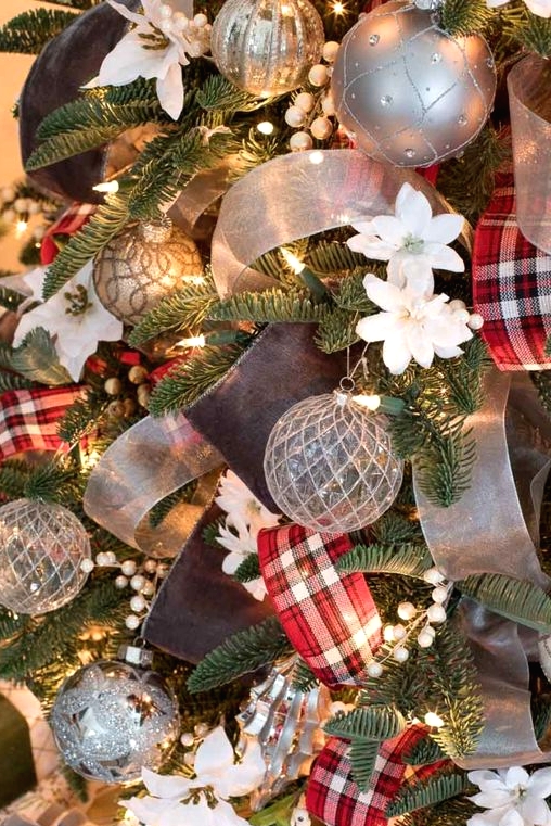 a Christmas tree decorated with lights, beads, faux white blooms, silver grey ornaments and red plaid and semi sheer ribbons is a gorgeous decoration