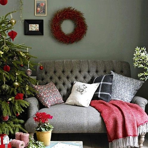 a red loveseat with red, grey and white pillows, a red blanket, a Christmas tree with red and green ornaments and a mini gallery wall