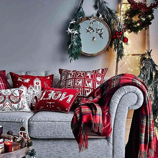 a refined grey and red Christmas space with a grey sofa, red printed pillows and a plaid blanket, evergreens, lights and stars on the walls
