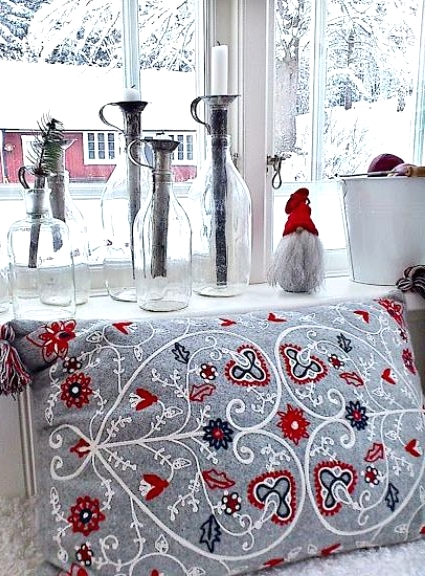 Scandi Christmas decor with a grey embroidered pillow, a gnome in a red hat, bottles with candleholders and evergreens