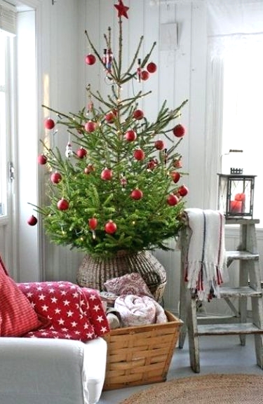 a Christmas tree in a basket with red ornaments all over, a basket with blankets and red printed pillows on the chair is a cool idea