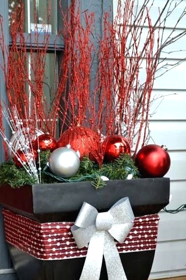an oversized black planter with a silver grey and grey ribbon bow, silver and red ornaments and red branches is a bold and pretty decoration