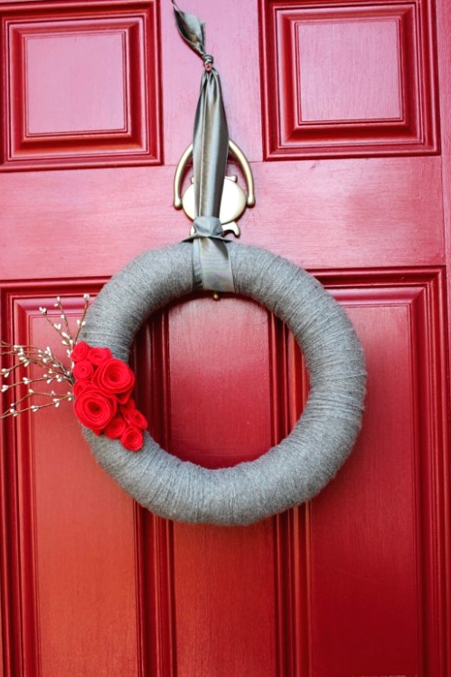 a red door with a grey yarn wrapped wreath with a bold red bloom and some blooming branches is a chic and bold idea