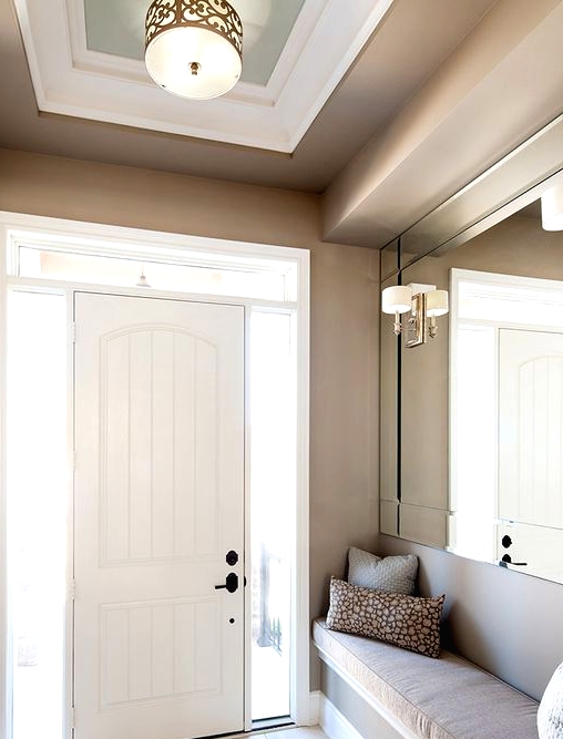 a chic greige entryway with an oversized mirror, lamps and a built-in greige upholstered bench is a lovely space to be