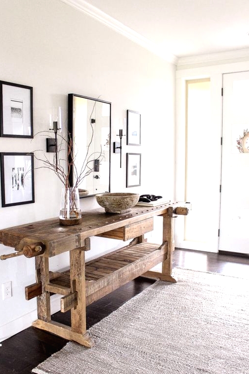 a delicate and airy greige entryway with a mini gallery wall with black frames, a stained vintage table, a neutral rug and lots of natural light