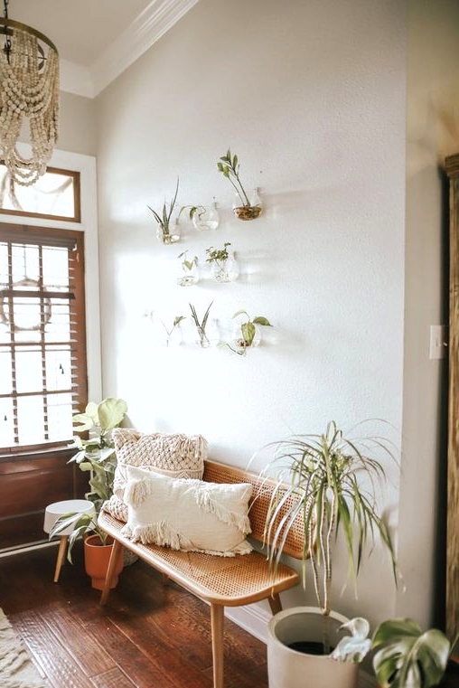a greige boho entryway with a cane bench, potted plants, a wooden bead chandelier, wall-mounted clear planters with greenery