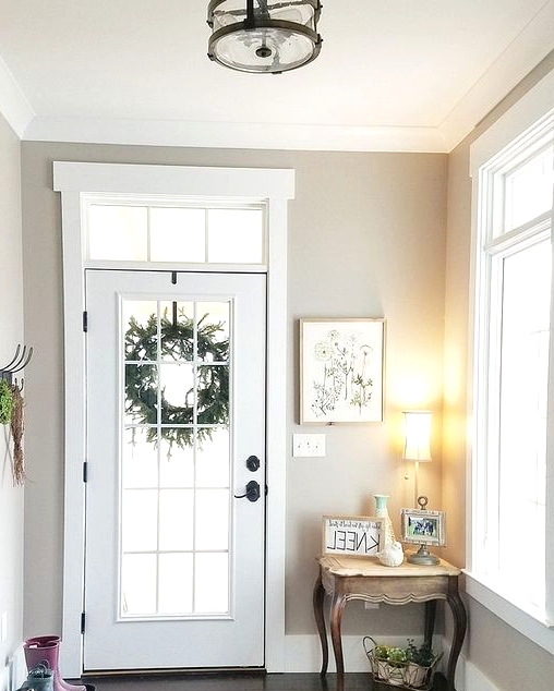 a greige entryway with lots of natural light, a vintage console table, a lamp, some greenery, an artwork and a rack