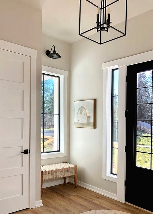 a lovely greige entryway with white doors and frames, a woven bench, a pendant lantern and a wall sconce is amazing