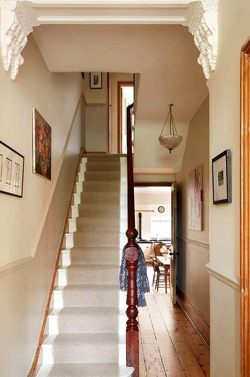 a small and cool greige entryway with wainscoting, artworks and vintage pendant lamps plus a greige carpet on the stairs
