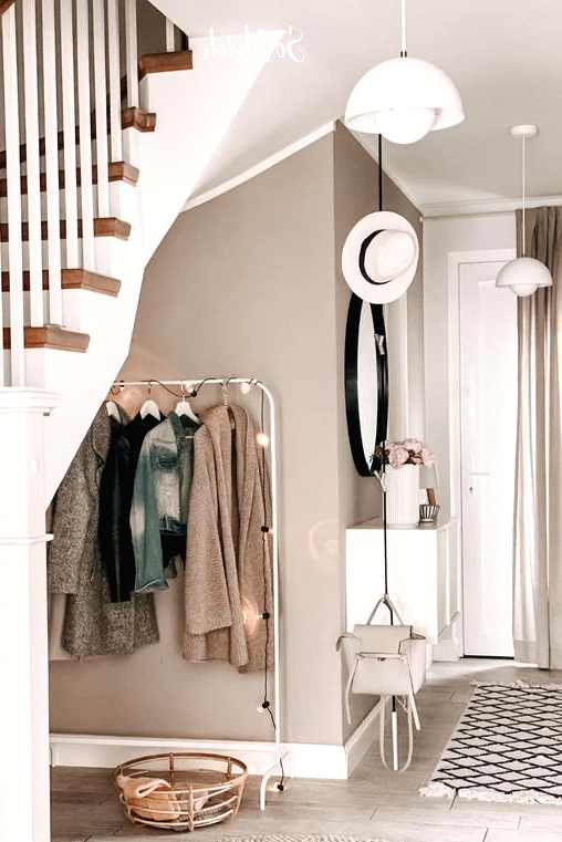 a welcoming greige entryway with a makeshift closet, a round mirror, a basket for storage, a white floating console table and pendant lamps