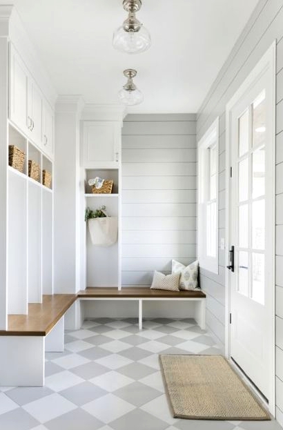 an elegant farmhouse greige mudroom with planked walls, white and stained storage furniture, a checked floor and lots of natural light