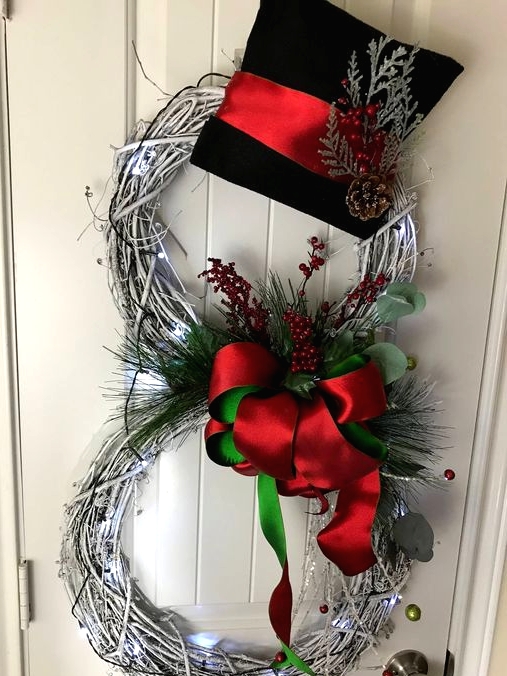 a snowman door decoration of white vine wreaths, green and red ribbons, a top hat and pinecones is a pretty idea to rock