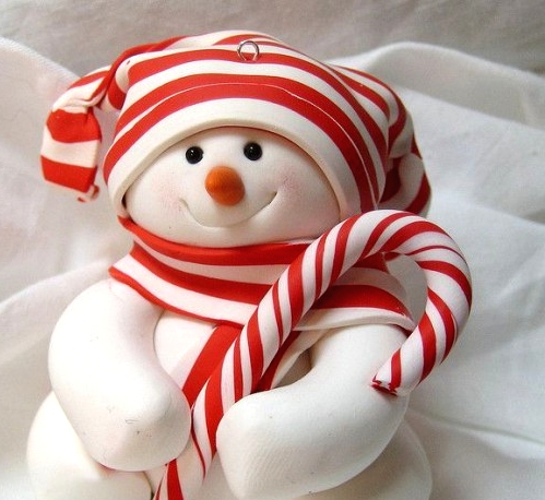 a pretty white snowman decoration with a candy and a striped hat and scarf that match and make the piece look bolder