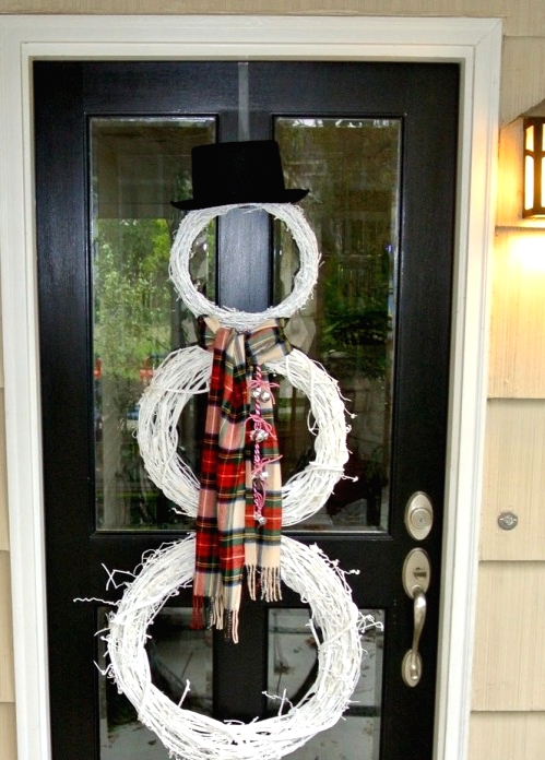 a white snowman made of white wreaths, a plaid scarf and a black top hat is a cool alternative to a usual Christmas wreath on your door