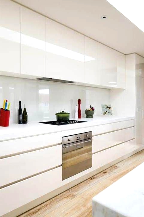 a modern creamy kitchen with sleek cabinets, white stone countertops and a white creamy backsplash for a catchy glossy touch