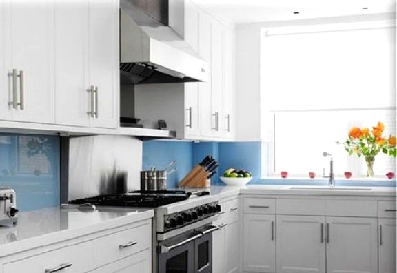 a modern white kitchen with shaker cabinets, white stone countertops and a blue glass backsplash for a touch of gloss and color