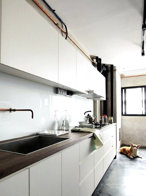 a modern white kitchen with sleek cabinets, dark stained butcherblock countertops and a white solid glass backsplash