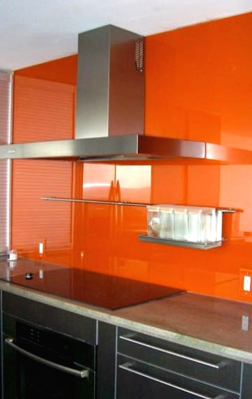a dramatic black modern kitchen with a bold orange soild glass backsplash for a contrasting touch