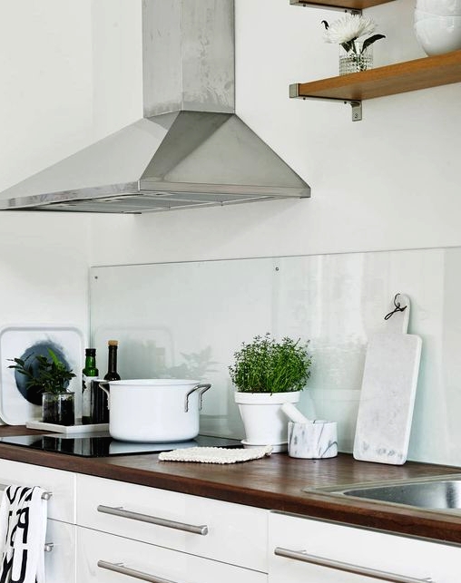 a white Scandinavian kitchen with dark-stained butcherblock countertops and a clear glass backsplash that helps to create a calm feel