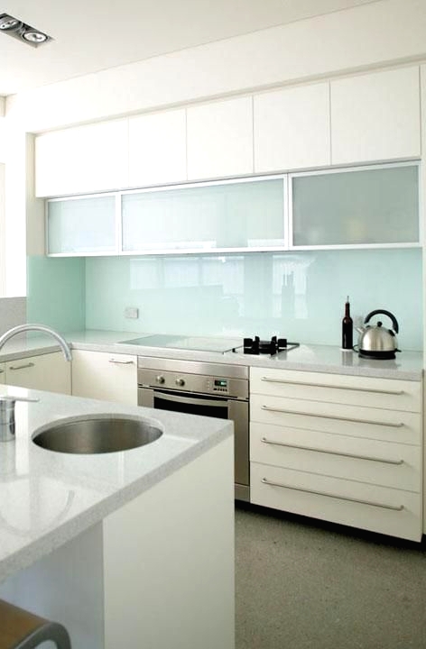 an airy white kitchen with white stone countertops, frosted glass cabinets and a mint glass backsplash is a lovely space