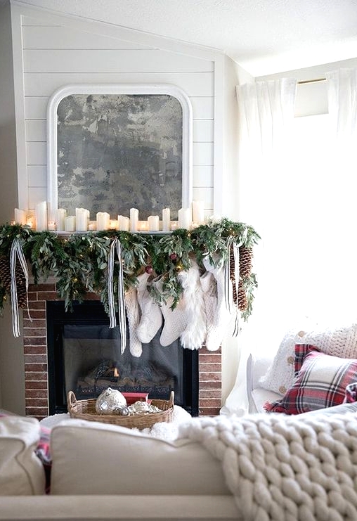 a Christmas mantel with an evergreen and light garland, pillar candles, striped ribbons and white stockings is a gorgeous idea
