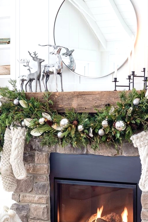 a cottage Christmas mantel with an evergreen, pinecone and ornament garland, neutral stockings, silver deer and candles in a black candelabra