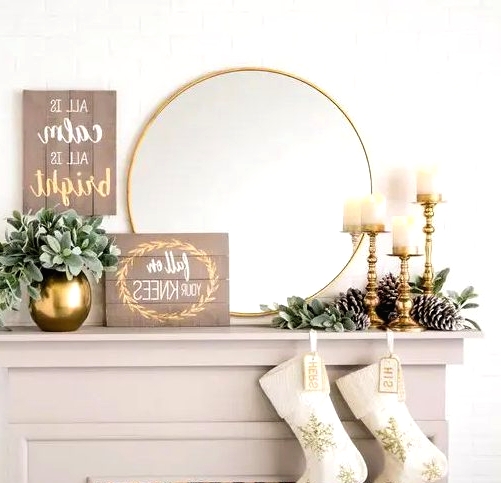 a glam and rustic Christmas mantel with large pinecones, gilded candle holders and a vase, a sign and a mirror