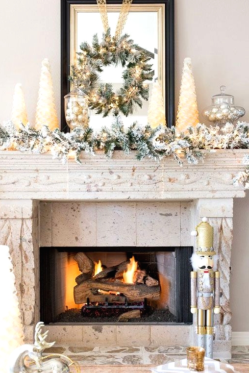 a lovely snowy Christmas mantel with a snowy evergreen garland with lights, mini Christmas trees and silver ornaments in jars