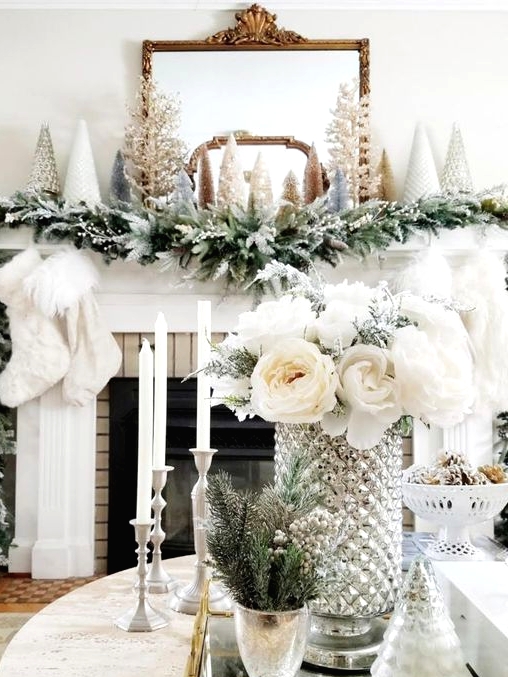 a winter wonderland mantel with a snowy evergreen garland, faux fur stockings, mini Christmas trees and a mirror in a chic frame