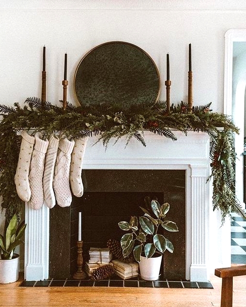 an all-natural Christmas mantel with a super lush evergreen and fern garland with pinecones, tall and thin candles, neutral stockings