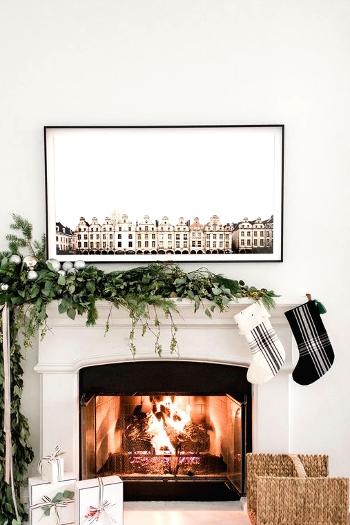 an ultra-modern Christmas mantel with a greenery and evergreen garland with silver ornaments, and a duo of black and white plaid stockings