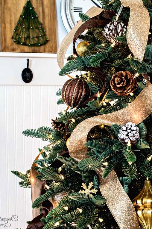 a gorgeous rustic and woodland glam Christmas tree with usual and snowy pinecone ornaments, fabric balls, lights, brown and gold glitter ribbons is wow