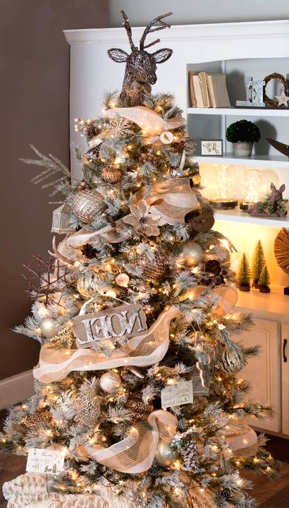 a creative woodland glam Christmas tree with lights, signs, metallic ornaments, branches, snowflakes and a deer head on top